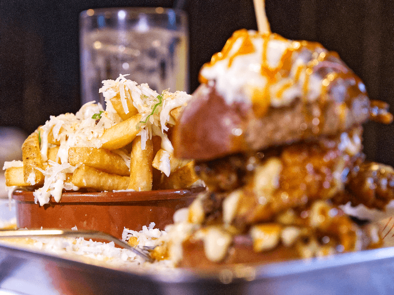 Stacked fried chicken burger topped with sauce, served with loaded fries